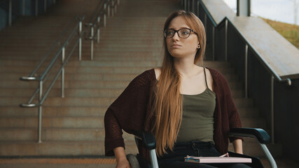 Sad helpless disabled young woman in front of the stairways in the wheelchair. inaccessible area. High quality photo