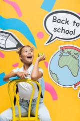 Excited kid with apple and book looking at speech bubble with back to school lettering and paper art on yellow background