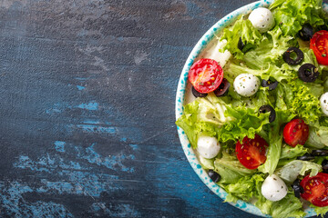 Fresh vegetables salad with tomatoes, mozzarella and black olives. Top view, text space