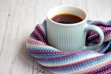 Blue cup of hot tea is wrapped in a warm striped multi-colored scarf. Autumn background with copy space