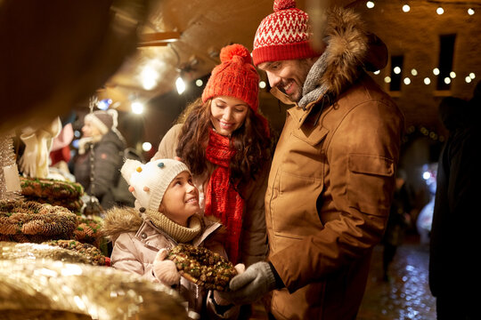 family, winter holidays and celebration concept - happy mother, father and little daughter buing wreath at christmas market on town hall square in tallinn, estonia