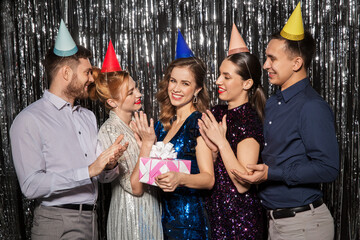 celebration, fun and holidays concept - happy friends in party hats with birthday gift applauding