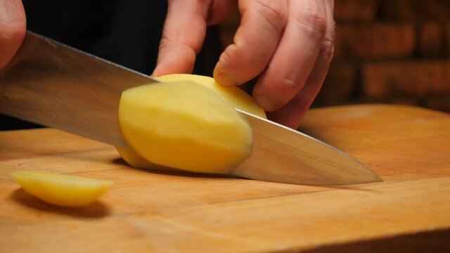 Closeup of hand with knife cutting potato.