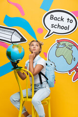 Fototapeta premium Pensive child holding globe near speech bubble with back to school lettering and paper art on yellow background