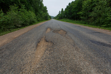 Very bad road in Russia. The asphalt road is all in holes in the middle of the forest.