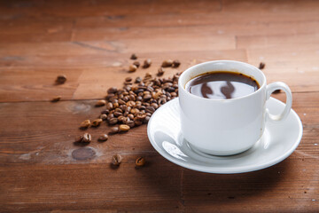 White cup of coffee on a wooden table next to a scattering of coffee beans.