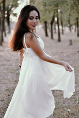 Long-haired brunette in a white dress in the woods