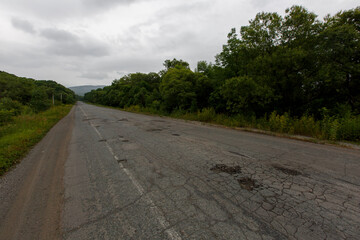 Very bad road in Russia. The asphalt road is all in holes in the middle of the forest.