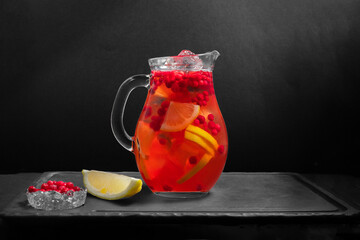 The glass jug with cold natural lemonades from oranges, cranberries are on a black background with slice lemon. Copy space.