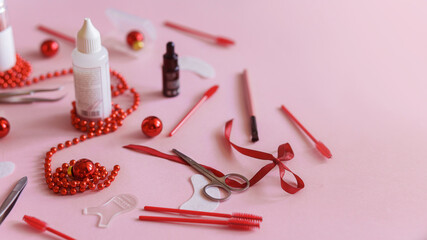 Beauty salon and lash artist tools and treatment products on left side lay out creating a frame on a pink background with a Christmas theme. Christmas tree toys with tools for treatment. Copy space.