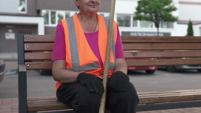 A cleaning lady on the street sits on a bench. Cleanliness and order in the yard during quarantine depends on the janitor.	
