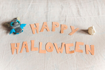 Frase con las palabras Happy Halloween en naranja sobre un fondo blanco con un murciélago y un fantasma © AliciaFdez