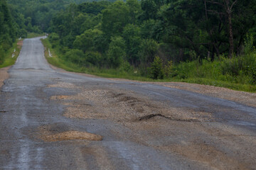 Fototapeta na wymiar Very bad road in Russia. The asphalt road is all in holes in the middle of the forest.