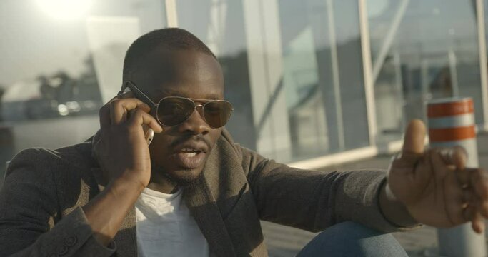 Habdsome african man in moden clothing is standing on the pole. He is trying to keep his balance while standing on the road pole. 4k footage.