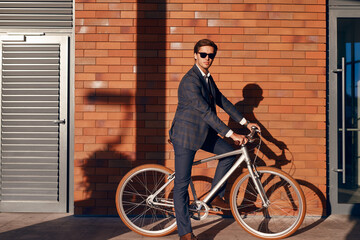 Fototapeta premium Confident businessman on bicycle near brick building