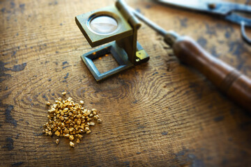 Inspecting gold. Gold nuggets with an vintage magnifying glass, with tools in background. intentionally shot with extremly shallow depth of field.