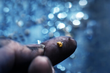 Discovery of gold. Gold on finger tips with shallow stream in background.Gold prospecting. Very...
