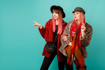 Fashionable studio shot of two stylish  models in bright winter or autumn   outfit, hat and scarf posing in turquoise  background.