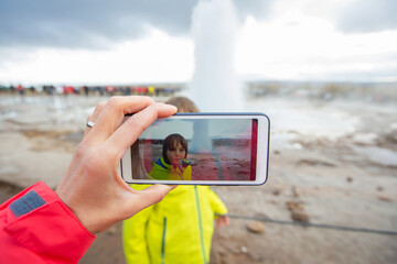 Mother recording video of her preschool son, boy enjoying the eruption of Strokkur Geysir in Iceland