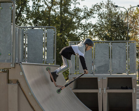 10-year-old boy in sportswear rides a scooter with half pipes. Trains at skatepark. the teenager is wearing a helmet on his head. Protect your child in extreme sports. Active lifestyle. Photo