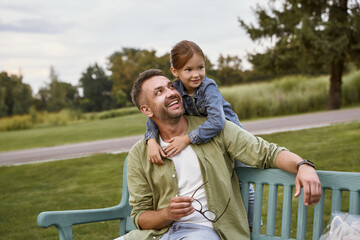 Spending time together outdoors. Portrait of happy loving father and cute little daughter sitting on the wooden bench in park, hugging and smiling