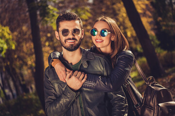 Photo of charming positive couple girl hug piggyback her boyfriend in september city park wear casual jacket