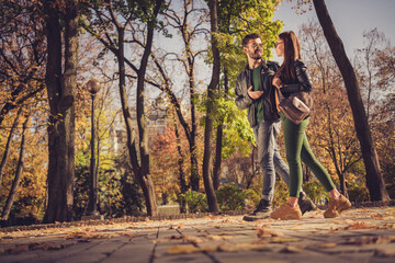 Obraz premium Full body profile side photo of positive couple go in autumn september town center park path speak wear jacket rucksack