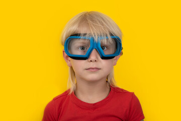 Portrait of blond boy in safety glasses on yellow background.