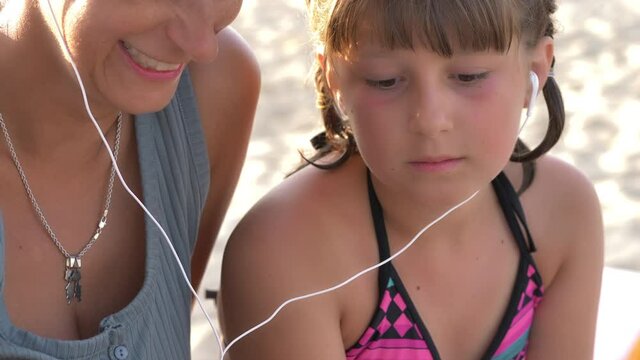 a mother and her daughters are making technology video call to friends  on a sandy beach with seaside in a sunny day during family vacation holidays.