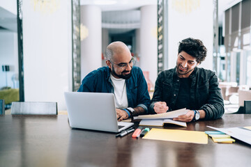 Two successful entrepreneurs collaborating on report analyzing sitting at table desktop and checking informative documents, Middle Eastern male employees brainstorming on financial statistics