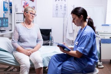 Nurse writing prescription on clipboard after consultation of elderly woman in hospital examination room. Converstation with medical stuff clinic medicine healthcare.