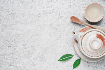 Tea concept with Creamy white tea set of cups and teapot surrounded with equipment and fresh tea leaves on concrete background with copy space.