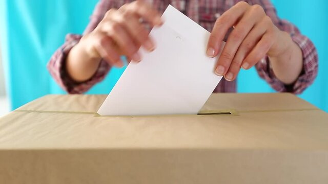 People put a paper ballot in a voting box at a polling station.