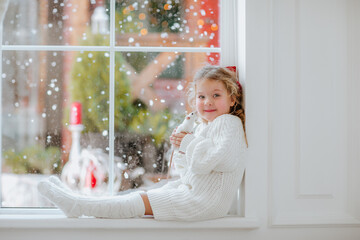 Young girl sitting near the big window holding white small rat. Snow background.