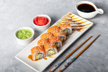 Sushi Sets Nigiri, Uramaki, California, Philadelphia, on a white plate. Nearby ginger and wasabi. Soy sauce in a white bowl. On a light gray background.