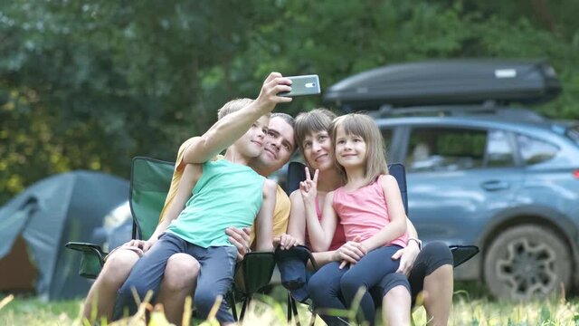 Parents and their children sitting together at campsite and taking selfie with mobile phone.