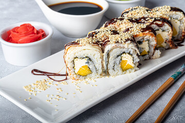 Sushi Sets Nigiri, Uramaki, California, Philadelphia, on a white plate. Nearby ginger and wasabi. Soy sauce in a white bowl. On a light gray background.