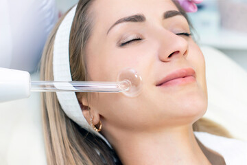 Cosmetologist performs a pulse current procedure for the face of a young woman. close