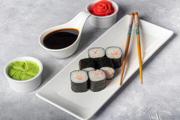 Sushi Sets Nigiri, Uramaki, California, Philadelphia, on a white plate. Nearby ginger and wasabi. Soy sauce in a white bowl. On a light gray background.