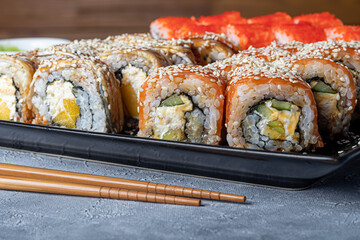 Sushi Sets Nigiri, Uramaki, California, Philadelphia, on a white plate. Nearby ginger and wasabi. Soy sauce in a white bowl. On a light gray background.