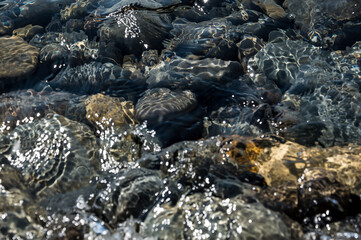 Large pebbles under water on The black sea coast. Splashes and sun glare.