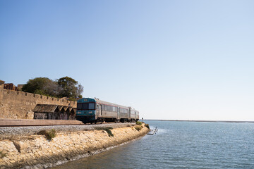 Train crossing the coast path on the shore of the Atlantic ocean in Faro, Algarve, Portugal