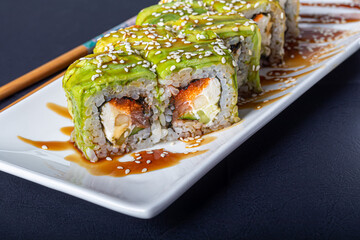 Sushi Sets Uramaki, California, Philadelphia, on a white plate. Nearby ginger and wasabi. Soy sauce in a white bowl. On a dark background.