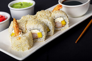 Sushi Sets Uramaki, California, Philadelphia, on a white plate. Nearby ginger and wasabi. Soy sauce in a white bowl. On a dark background.