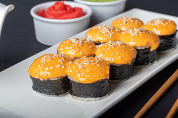 Sushi Sets Uramaki, California, Philadelphia, on a white plate. Nearby ginger and wasabi. Soy sauce in a white bowl. On a dark background.