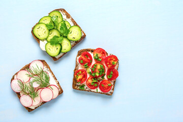 Variety of sandwiches for breakfast - slice of whole grain dark bread, red pepper, cream cheese, cucumbers, radishes, cherry tomatoes, garnished with dill, green onions on blue table Top view Flat lay