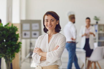 Happy successful business lady or company employee standing in office looking at camera and smiling - obrazy, fototapety, plakaty