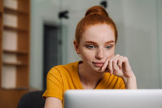 Image of serious beautiful redhead girl using laptop while working