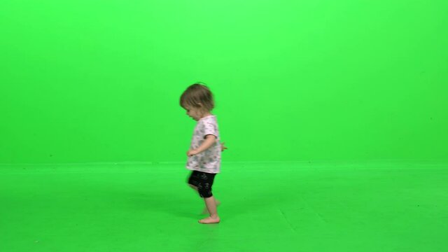Happy toddler girl smiling and dancing, going around in circles. Nodding at the end to stop, over green screen.