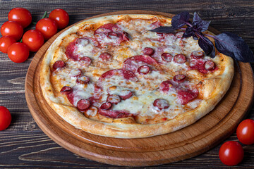 Pizza with bacon and herbs on a wooden plate with cheese and cherry tomatoes. On a wooden background.